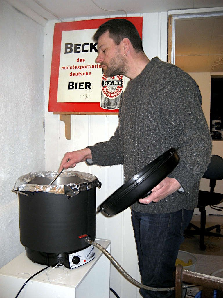 En hjemmebrygger står i kjellereen og rører i en liten bryggekjele.